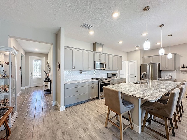 655 Conservation Blvd, Groveland, FL 34736 - kitchen with stainless steel appliances, gray cabinetry, a breakfast bar, decorative backsplash, and light stone counters