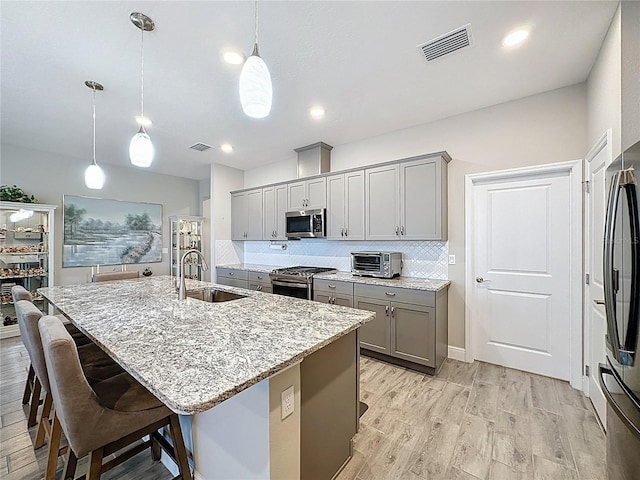 655 Conservation Blvd, Groveland, FL 34736 - kitchen featuring gray cabinetry, appliances with stainless steel finishes, decorative backsplash, light stone countertops, and a kitchen breakfast bar