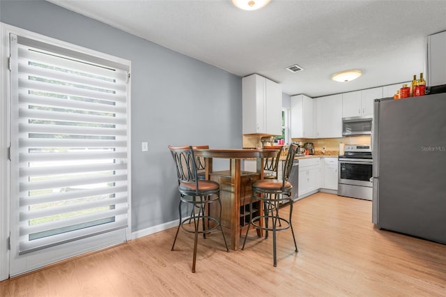 323 Savage Way, Groveland, FL 34736 - kitchen with stainless steel appliances, plenty of natural light, light wood-type flooring, white cabinets, and a textured ceiling