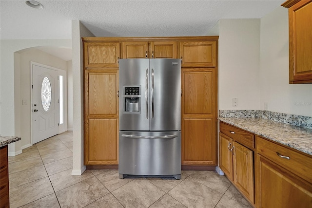 2880 Manor Downs, The Villages, FL 32162 - kitchen featuring stainless steel refrigerator with ice dispenser, brown cabinets, arched walkways, and a textured ceiling