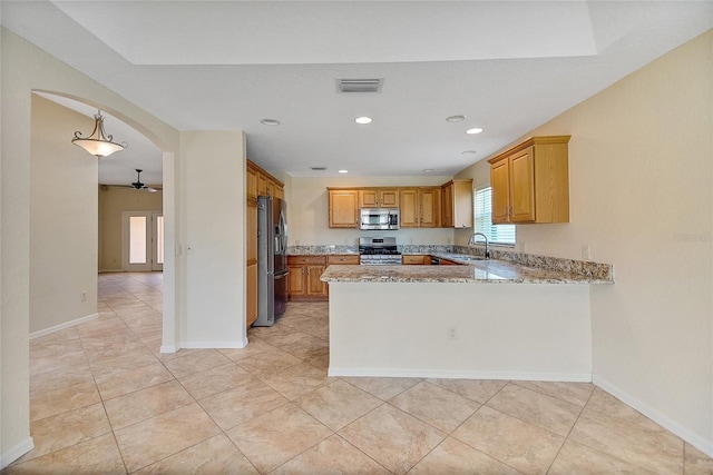 2880 Manor Downs, The Villages, FL 32162 - kitchen featuring appliances with stainless steel finishes, a peninsula, light stone countertops, ceiling fan, and brown cabinets