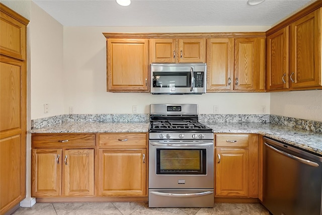 2880 Manor Downs, The Villages, FL 32162 - kitchen featuring appliances with stainless steel finishes, light stone counters, brown cabinetry, and light tile patterned flooring