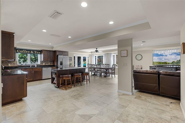 628 Drew Ave, Clermont, FL 34711 - kitchen with appliances with stainless steel finishes, a tray ceiling, dark countertops, a breakfast bar, and a kitchen island