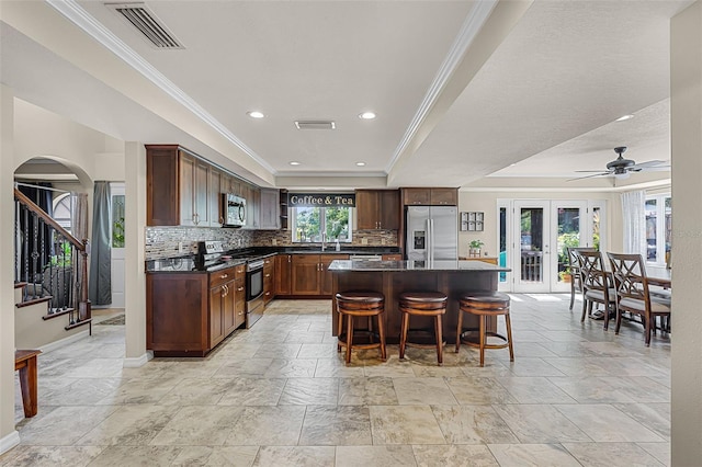 628 Drew Ave, Clermont, FL 34711 - kitchen featuring stainless steel appliances, dark countertops, crown molding, backsplash, and a kitchen bar