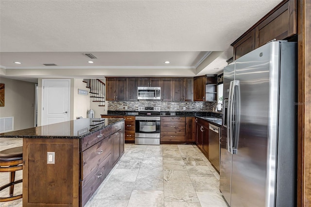 628 Drew Ave, Clermont, FL 34711 - kitchen featuring appliances with stainless steel finishes, a tray ceiling, decorative backsplash, a kitchen island, and dark stone countertops