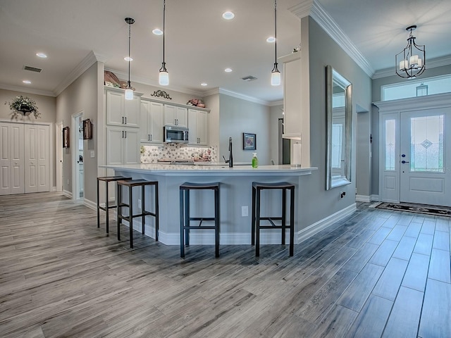 6295 Danielson Loop, The Villages, FL 32163 - kitchen with stainless steel microwave, a breakfast bar area, light wood finished floors, white cabinetry, and recessed lighting
