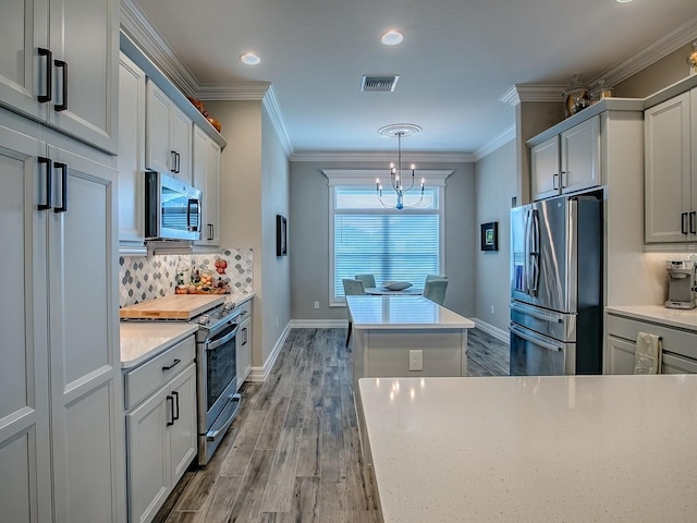 6295 Danielson Loop, The Villages, FL 32163 - kitchen featuring appliances with stainless steel finishes, wood finished floors, a chandelier, light countertops, and crown molding