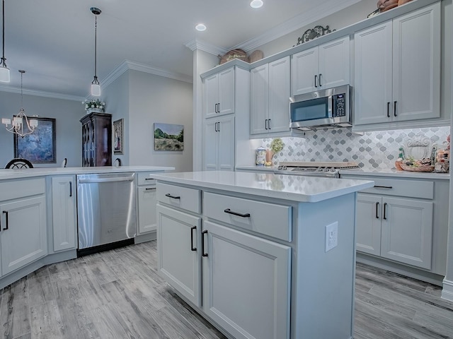 6295 Danielson Loop, The Villages, FL 32163 - kitchen with appliances with stainless steel finishes, a kitchen island, light wood-type flooring, crown molding, and light countertops