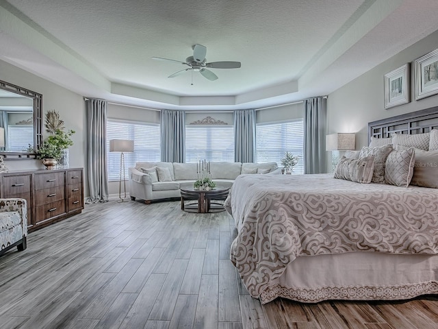 6295 Danielson Loop, The Villages, FL 32163 - bedroom with a tray ceiling, multiple windows, wood finished floors, a ceiling fan, and a textured ceiling
