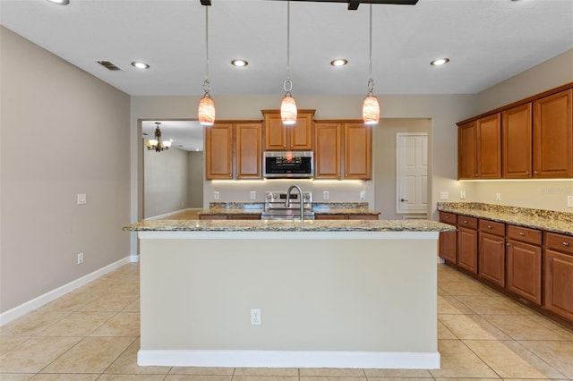 1892 Sanderling Dr, Clermont, FL 34711 - kitchen featuring appliances with stainless steel finishes, light stone counters, brown cabinetry, a kitchen island with sink, and recessed lighting