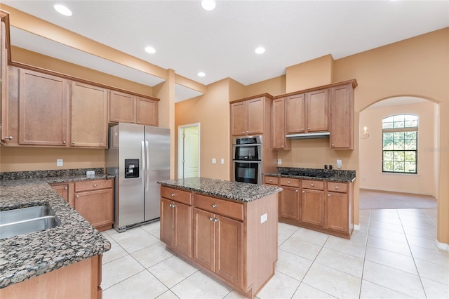 21312 Marsh View Ct, Clermont, FL 34715 - kitchen featuring appliances with stainless steel finishes, a kitchen island, light tile patterned floors, arched walkways, and dark stone counters