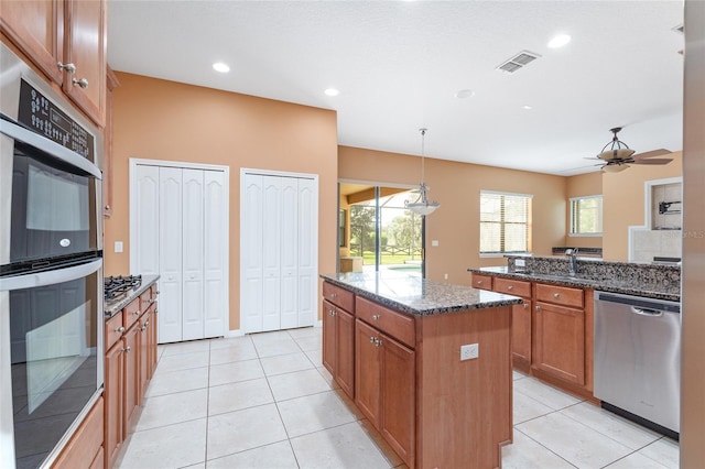 21312 Marsh View Ct, Clermont, FL 34715 - kitchen with stainless steel appliances, brown cabinetry, a kitchen island, dark stone counters, and light tile patterned floors
