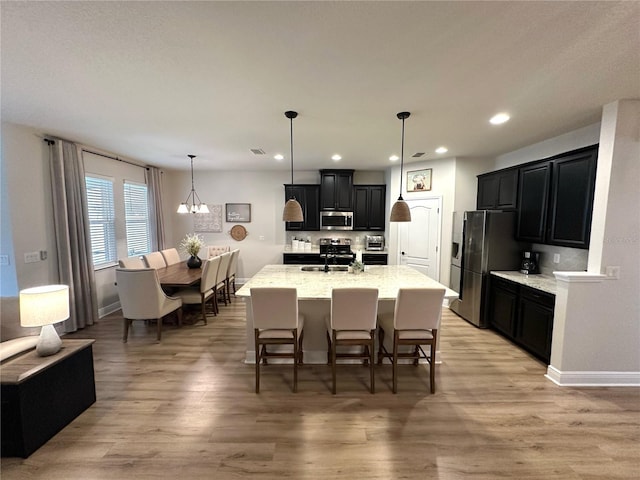 384 Summer Squall Rd, Davenport, FL 33837 - kitchen with appliances with stainless steel finishes, dark cabinets, a kitchen bar, light wood-style flooring, and recessed lighting