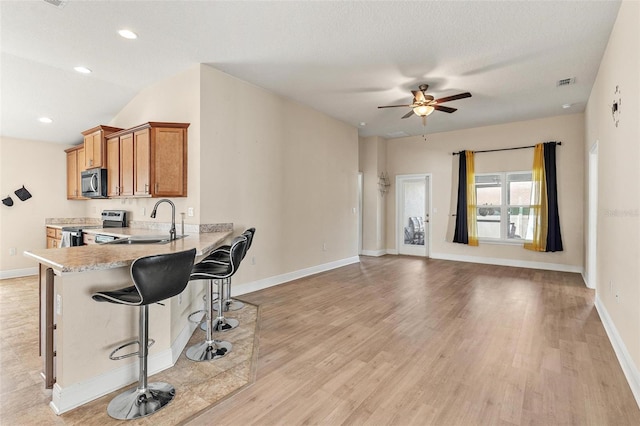 7732 Sloewood Dr, Leesburg, FL 34748 - kitchen featuring appliances with stainless steel finishes, brown cabinets, ceiling fan, a kitchen bar, and light wood-type flooring
