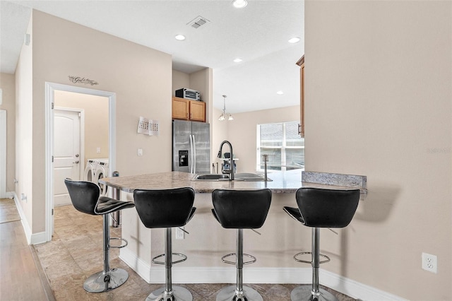 7732 Sloewood Dr, Leesburg, FL 34748 - kitchen with stainless steel fridge, washing machine and dryer, a peninsula, a kitchen breakfast bar, and recessed lighting