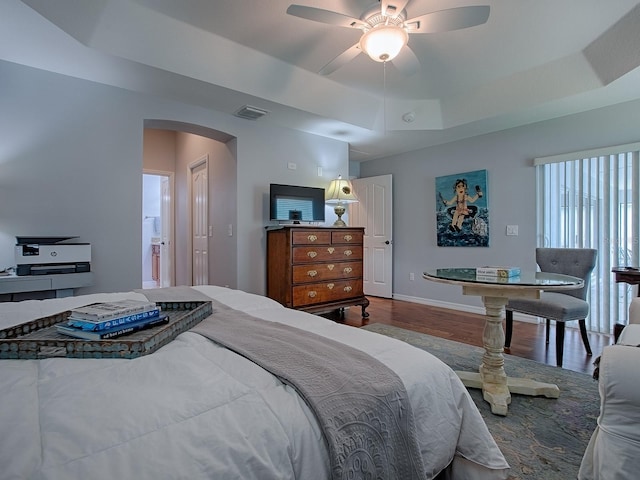 1982 Eldridge Loop, The Villages, FL 32162 - bedroom featuring a tray ceiling, wood finished floors, arched walkways, a ceiling fan, and ensuite bathroom