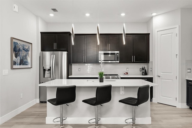 2163 White Feather Loop, Oakland, FL 34787 - kitchen featuring appliances with stainless steel finishes, an island with sink, light countertops, light wood finished floors, and decorative backsplash