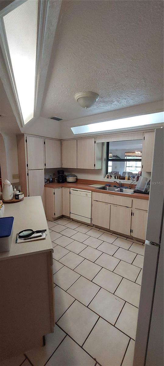 13420 Debbie Ln, Clermont, FL 34715 - kitchen featuring white dishwasher, light tile patterned floors, freestanding refrigerator, a textured ceiling, and a skylight