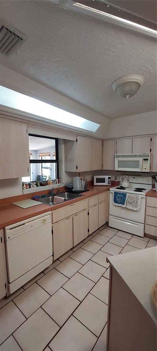 13420 Debbie Ln, Clermont, FL 34715 - kitchen with white appliances, a skylight, light tile patterned floors, a textured ceiling, and light countertops