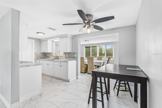 11326 Yellowwood Ln, Port Richey, FL 34668 - kitchen with light marble finish flooring, white cabinets, ceiling fan, and decorative backsplash