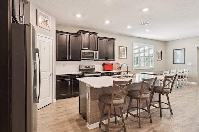 49 White Horse Way, Groveland, FL 34736 - kitchen featuring appliances with stainless steel finishes, light countertops, a breakfast bar, light wood-style floors, and an island with sink