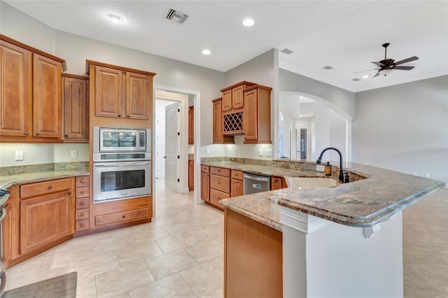 18139 Great Blue Heron Dr, Groveland, FL 34736 - kitchen featuring stainless steel appliances, a peninsula, stone counters, arched walkways, and brown cabinets