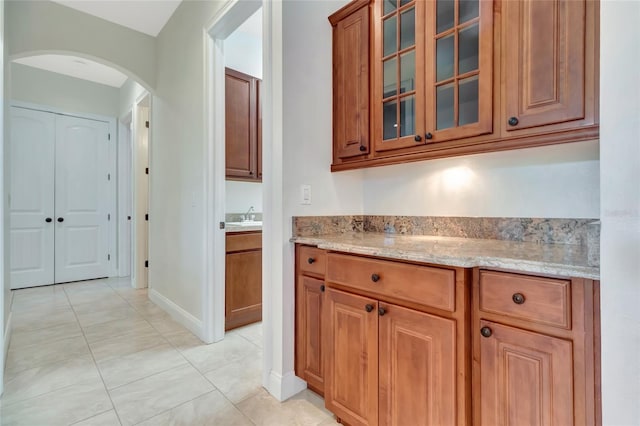 18139 Great Blue Heron Dr, Groveland, FL 34736 - kitchen featuring arched walkways, brown cabinets, light stone counters, and glass insert cabinets