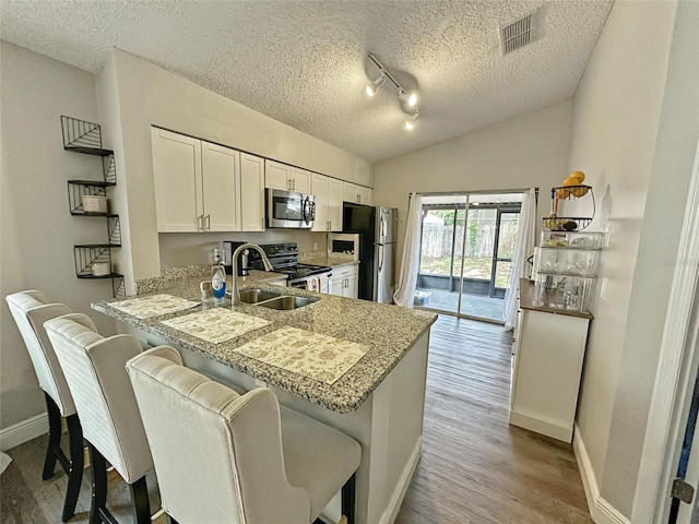 7047 Hickory Branch Cir, Orlando, FL 32818 - kitchen with stainless steel appliances, a textured ceiling, white cabinetry, wood finished floors, and a breakfast bar
