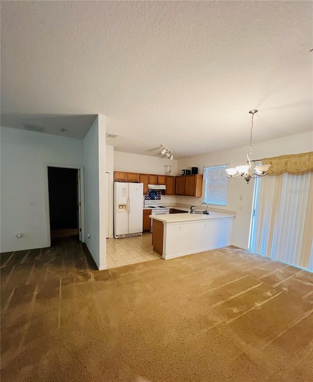 kitchen featuring white appliances, brown cabinetry, light colored carpet, a chandelier, and a peninsula