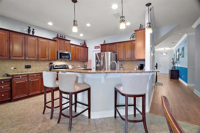 30230 Tokara Ter, Mount Dora, FL 32757 - kitchen with stainless steel appliances, a kitchen breakfast bar, decorative backsplash, light stone counters, and decorative light fixtures