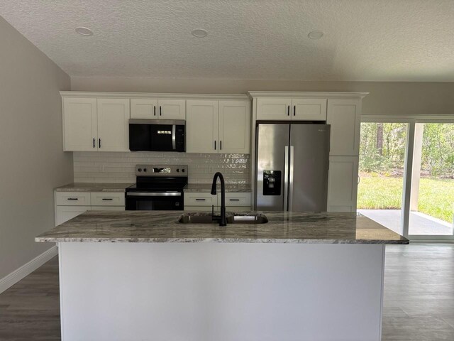 6805 N Sandborn Loop, Citrus Springs, FL 34433 - kitchen with appliances with stainless steel finishes, white cabinets, tasteful backsplash, a textured ceiling, and a kitchen island with sink