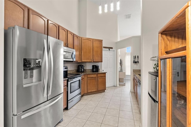 1532 Nightfall Dr, Clermont, FL 34711 - kitchen featuring stainless steel appliances, light tile patterned floors, a towering ceiling, brown cabinets, and decorative light fixtures