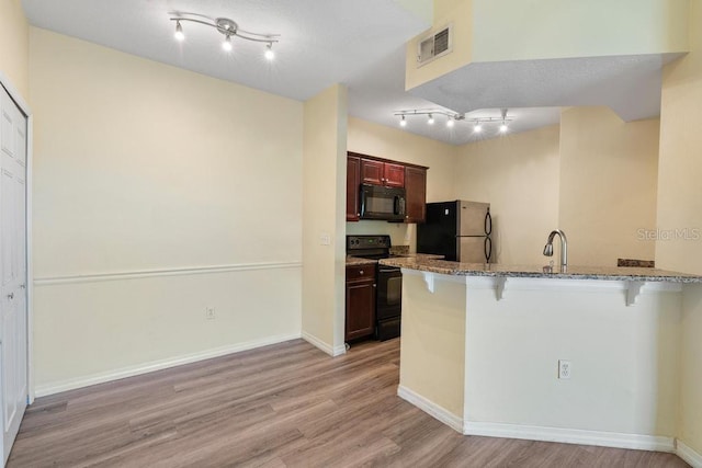 5518 Metrowest Blvd Unit 11-302, Orlando, FL 32811 - kitchen featuring black appliances, a breakfast bar area, light wood-type flooring, stone counters, and a peninsula