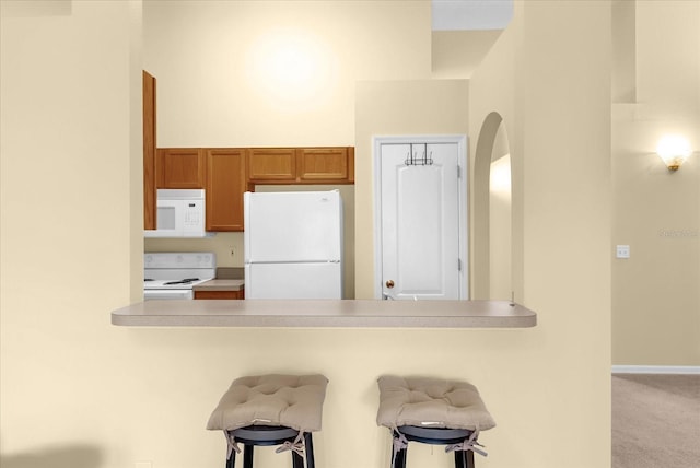 637 Harbor Villa Ct, Clermont, FL 34711 - kitchen featuring white appliances, a peninsula, a breakfast bar area, brown cabinets, and arched walkways