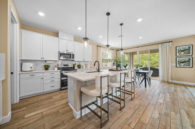 3916 Southern Vista Loop, Saint Cloud, FL 34772 - kitchen featuring stainless steel appliances, light wood finished floors, light countertops, a kitchen island with sink, and decorative backsplash