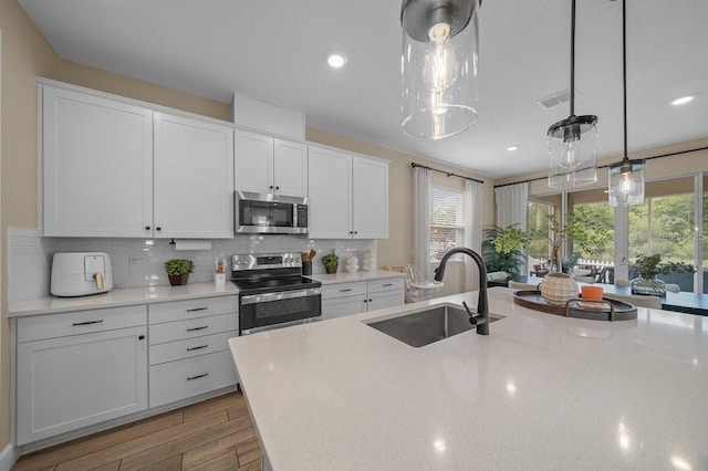 3916 Southern Vista Loop, Saint Cloud, FL 34772 - kitchen with appliances with stainless steel finishes, light wood-style floors, white cabinets, decorative backsplash, and hanging light fixtures