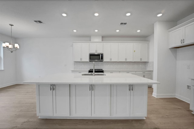 983 Fiesta Key Cir, Lady Lake, FL 32159 - kitchen with stainless steel microwave, white cabinets, an island with sink, tasteful backsplash, and a chandelier