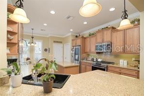 370 Salt Marsh Ln, Groveland, FL 34736 - kitchen featuring stainless steel microwave, stove, crown molding, brown cabinetry, and fridge