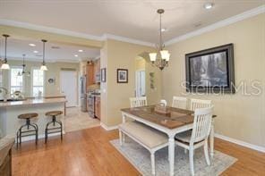 370 Salt Marsh Ln, Groveland, FL 34736 - dining room featuring arched walkways, crown molding, light wood-type flooring, and a chandelier