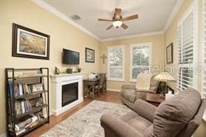 370 Salt Marsh Ln, Groveland, FL 34736 - living area with crown molding, a glass covered fireplace, wood finished floors, and a ceiling fan