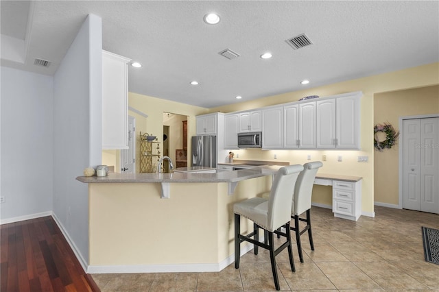 7811 Laurel View Dr, Mount Dora, FL 32757 - kitchen with stainless steel appliances, a peninsula, a kitchen bar, white cabinetry, and recessed lighting