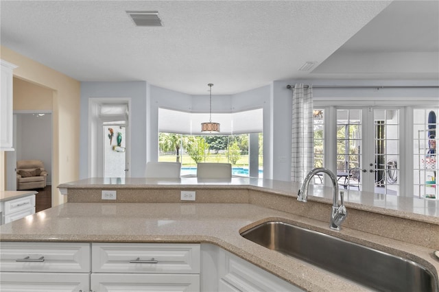 7811 Laurel View Dr, Mount Dora, FL 32757 - kitchen with french doors, white cabinets, light stone counters, a textured ceiling, and pendant lighting