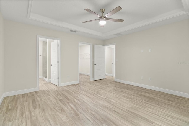 671 E Toledo Dr, Citrus Springs, FL 34434 - unfurnished bedroom featuring a tray ceiling, light wood-style floors, a spacious closet, and ensuite bath