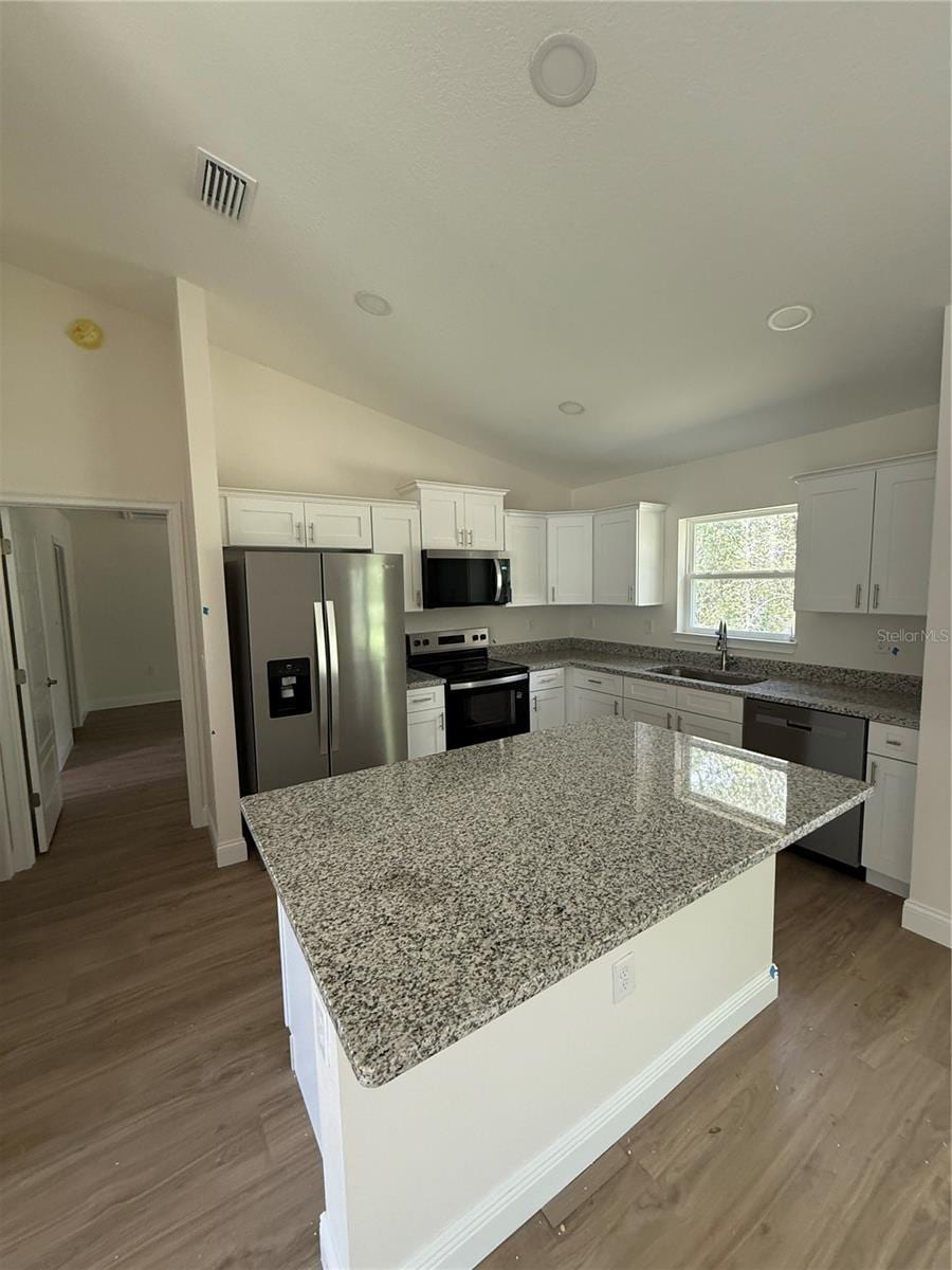 675 E Toledo Dr, Citrus Springs, FL 34434 - kitchen with appliances with stainless steel finishes, white cabinetry, vaulted ceiling, a kitchen island, and wood finished floors