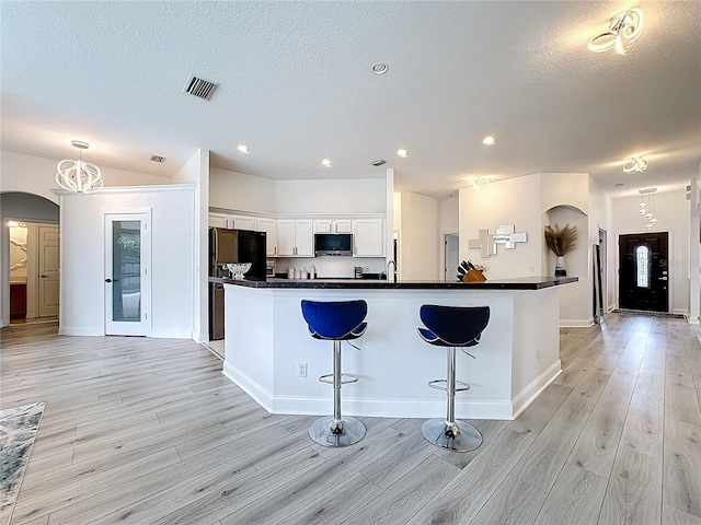2421 Cimmaron Ash Way, Apopka, FL 32703 - kitchen with arched walkways, stainless steel microwave, dark countertops, light wood-style flooring, and white cabinets