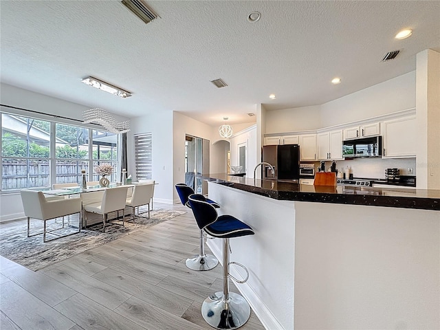 2421 Cimmaron Ash Way, Apopka, FL 32703 - kitchen featuring black fridge, white cabinetry, light wood-type flooring, a breakfast bar area, and a textured ceiling