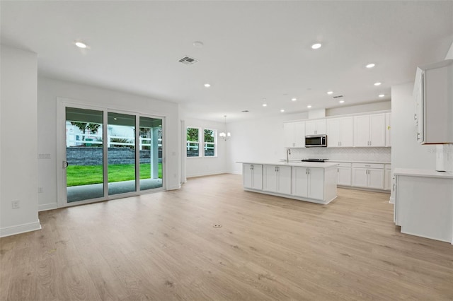 991 Fiesta Key Cir, Lady Lake, FL 32159 - kitchen featuring stainless steel microwave, decorative backsplash, light wood-style flooring, an island with sink, and white cabinets