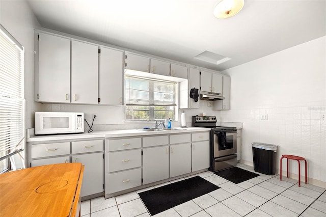 750 N Kentucky Ave, Umatilla, FL 32784 - kitchen featuring white microwave, stainless steel range with electric stovetop, under cabinet range hood, light tile patterned flooring, and light countertops