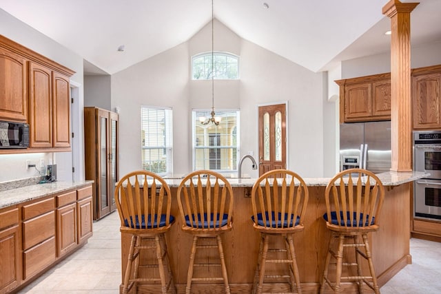 kitchen with light stone countertops, light tile flooring, an inviting chandelier, appliances with stainless steel finishes, and a breakfast bar area