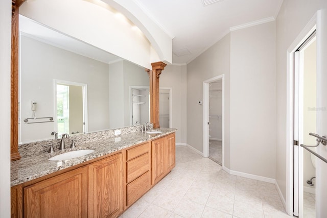 bathroom featuring tile flooring, dual sinks, oversized vanity, decorative columns, and ornamental molding